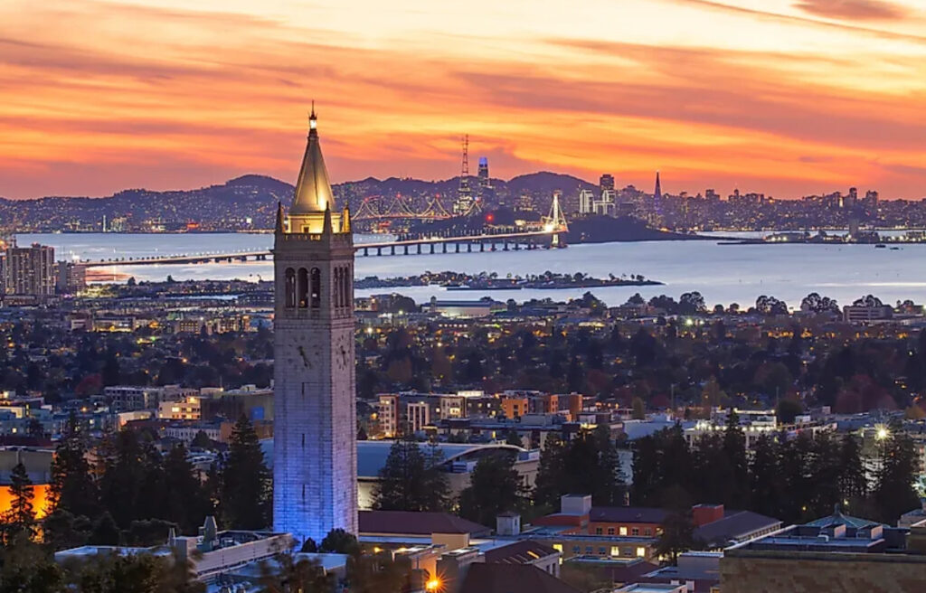 View of UC Berkeley's iconic Campanile with Berkeley in the foreground and San Francisco Bay at sunset